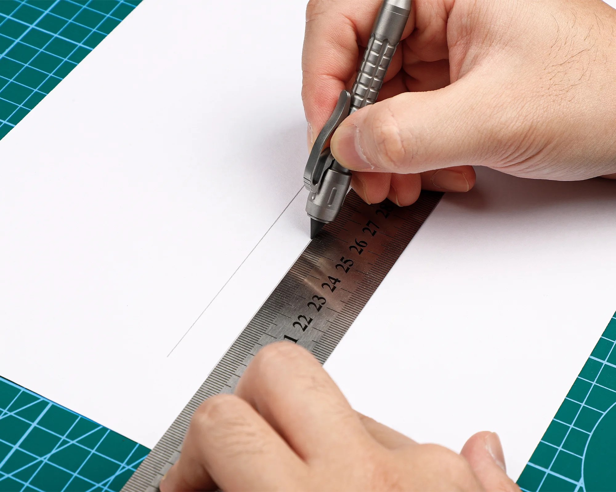 Hands using a metal ruler and mechanical pencil to draw a straight line on white paper over a green cutting mat.