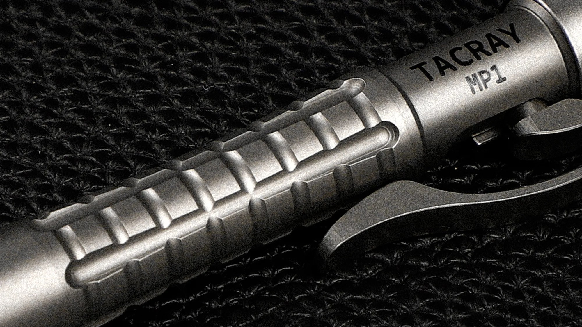 Close-up of a metallic Tacray MP1 pen with a textured grip and clip on a black woven surface.