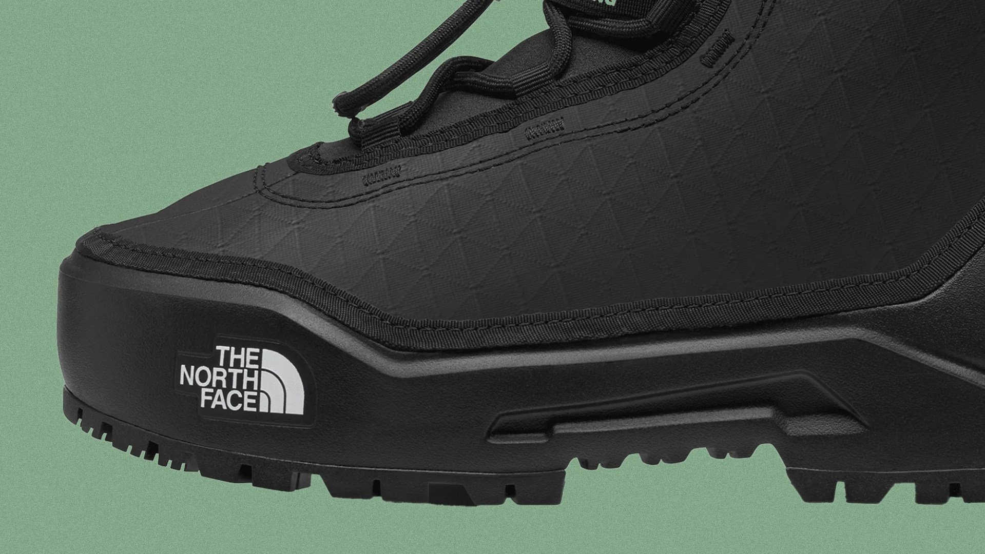 Close-up of a black The North Face hiking shoe with textured upper and rugged sole on a green background.
