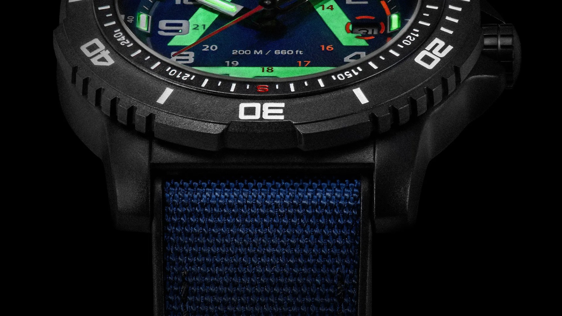Close-up of a black watch bezel with white markings and a blue woven fabric strap.