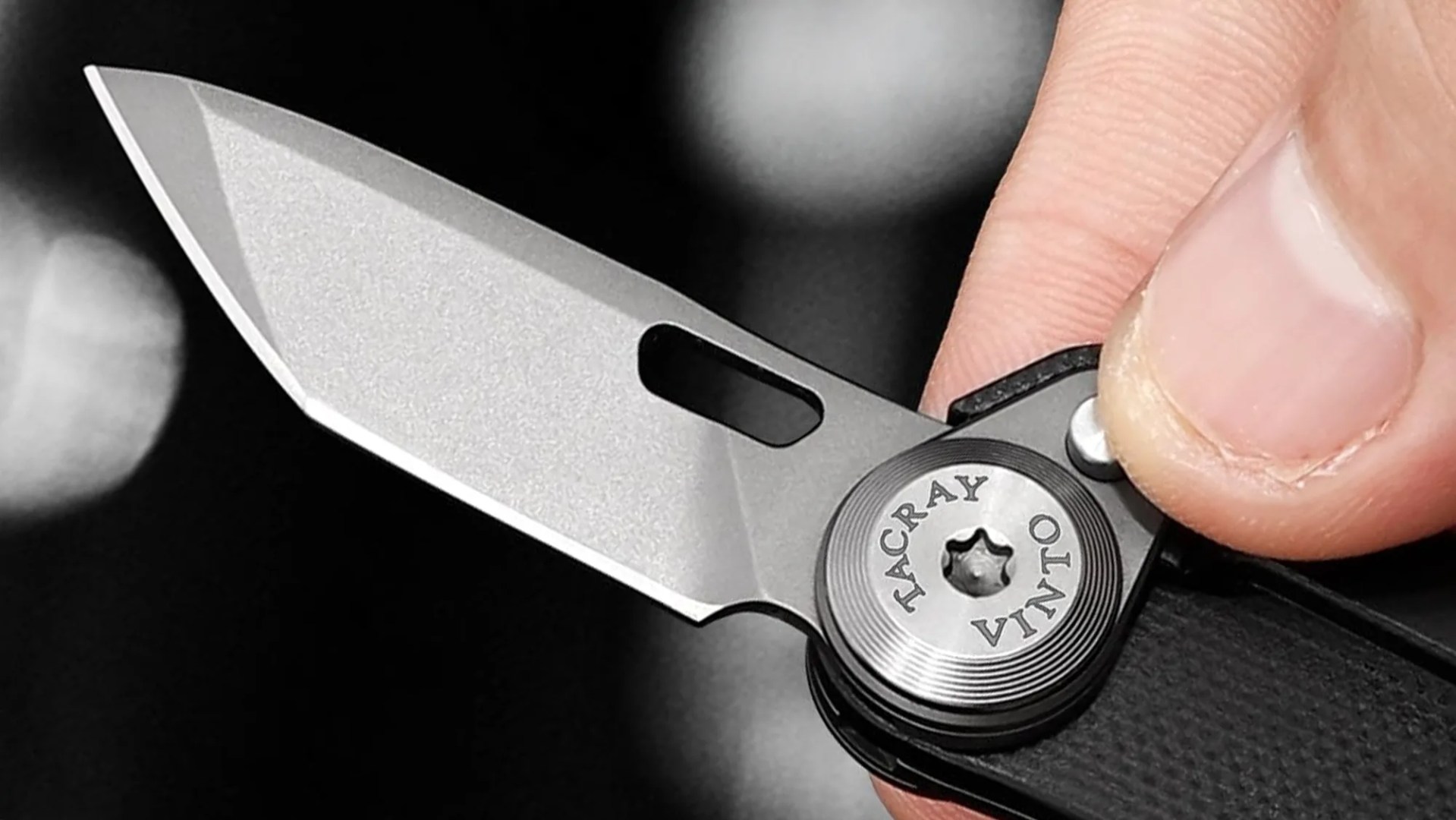 Close-up of a silver Tacray Vinto folding knife blade held by a hand.