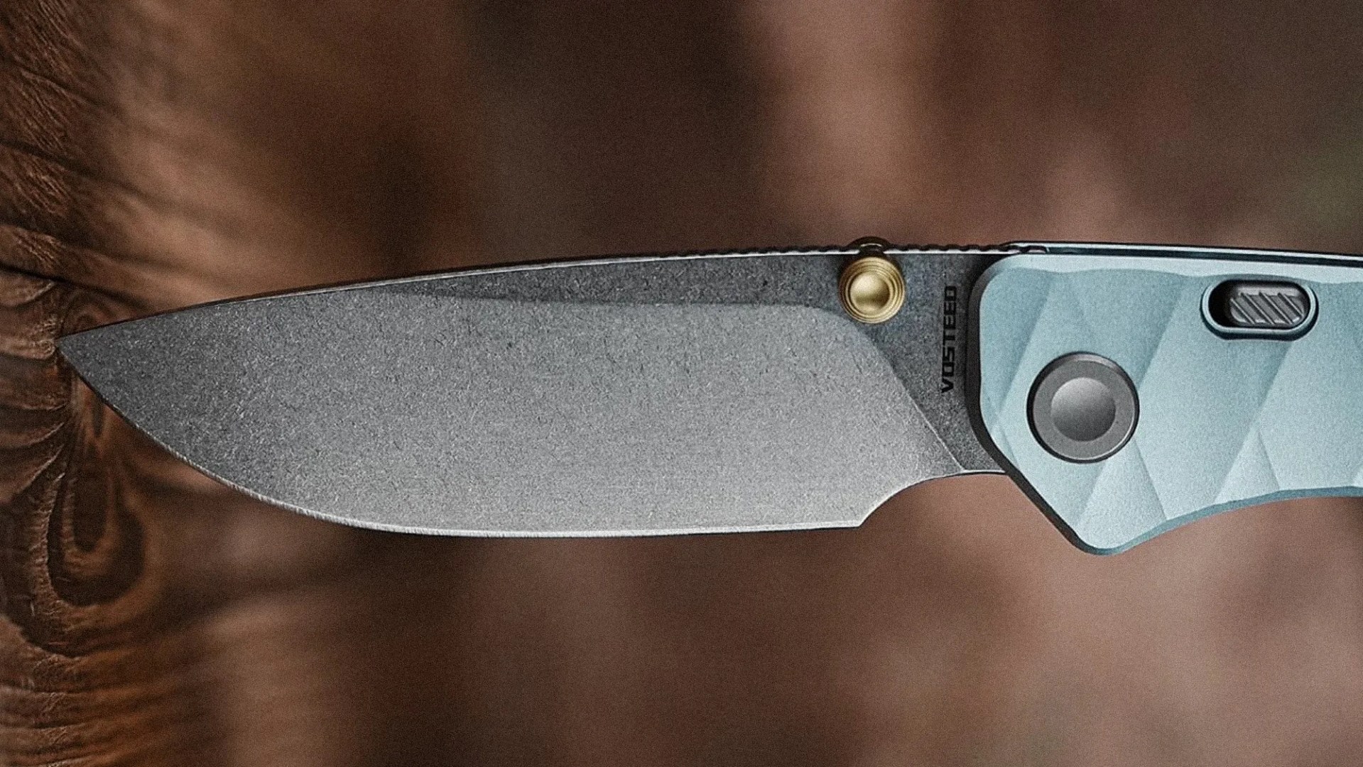Stonewashed folding knife blade with a blue textured handle and a brass thumb stud.