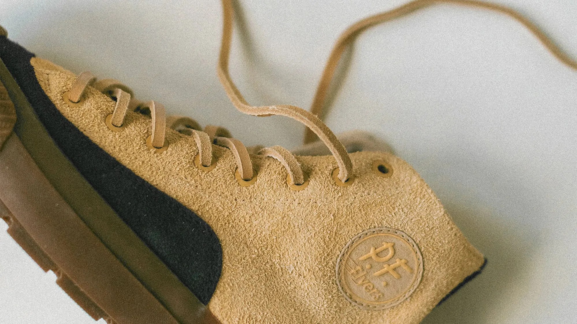 Tan suede sneaker with black stripe and brown sole, featuring "p.f. flyers" logo patch on the side.