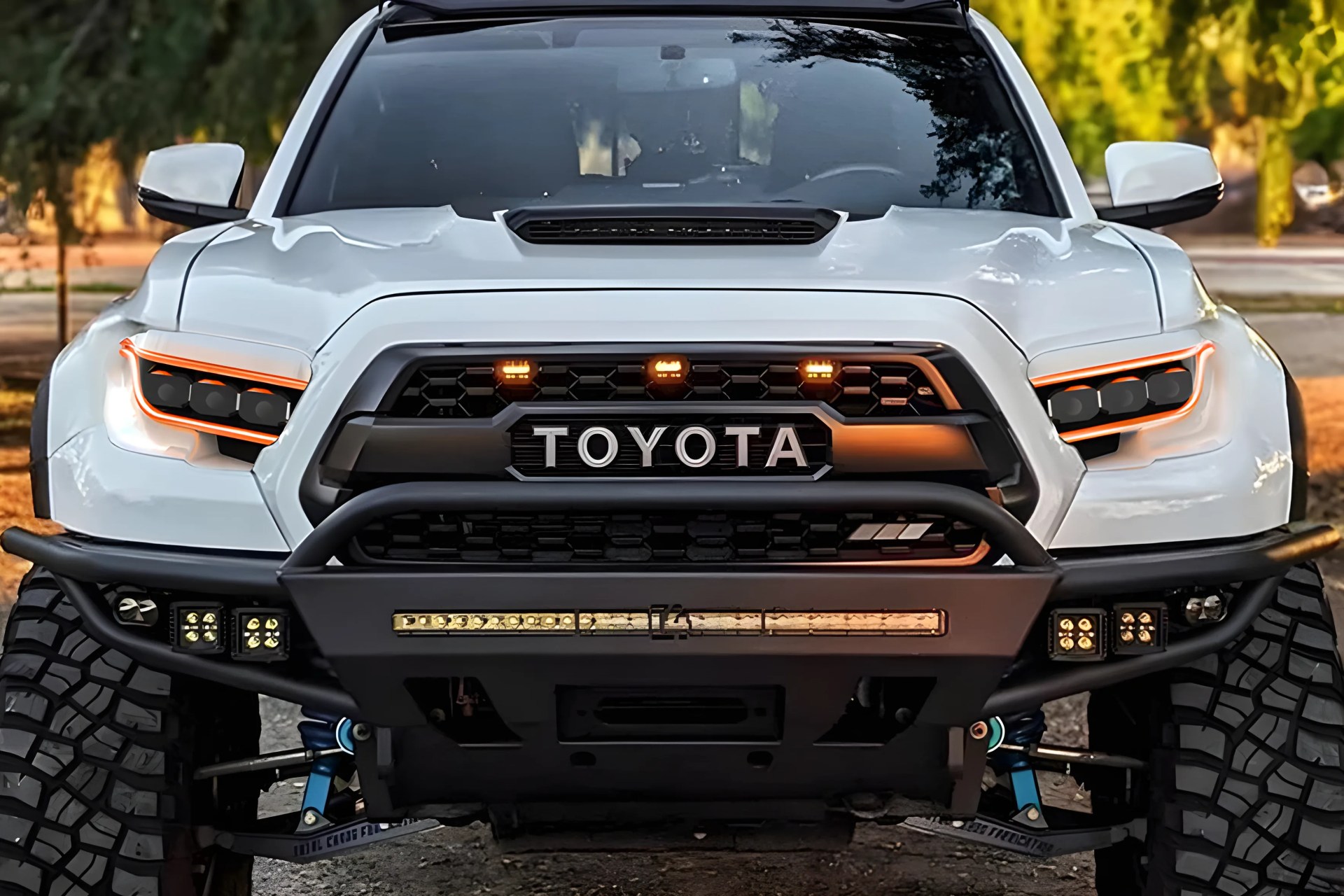 Front view of a white Toyota truck with black grille, orange-accented headlights, and off-road bumper with LED lights.