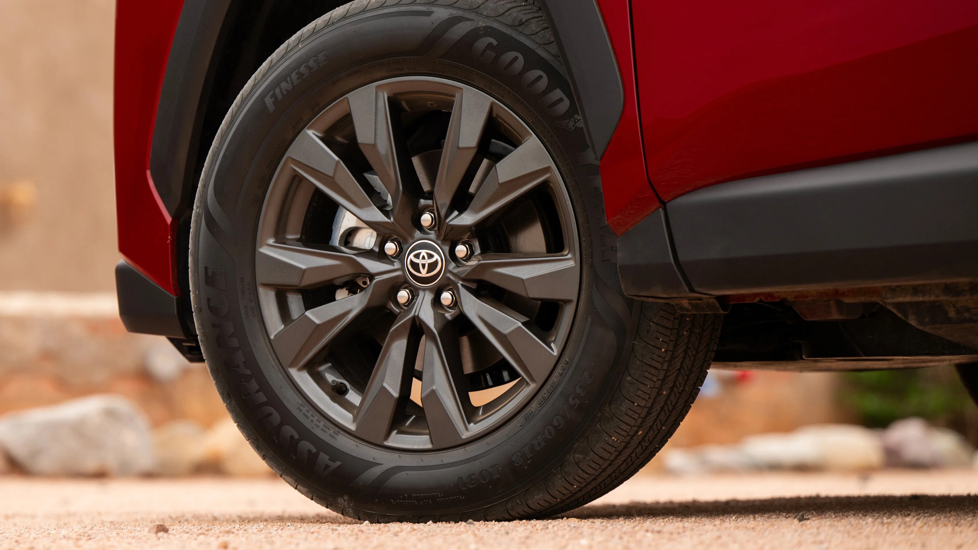 Black multi-spoke alloy wheel with Toyota logo on a red vehicle with Goodyear Assurance tire.