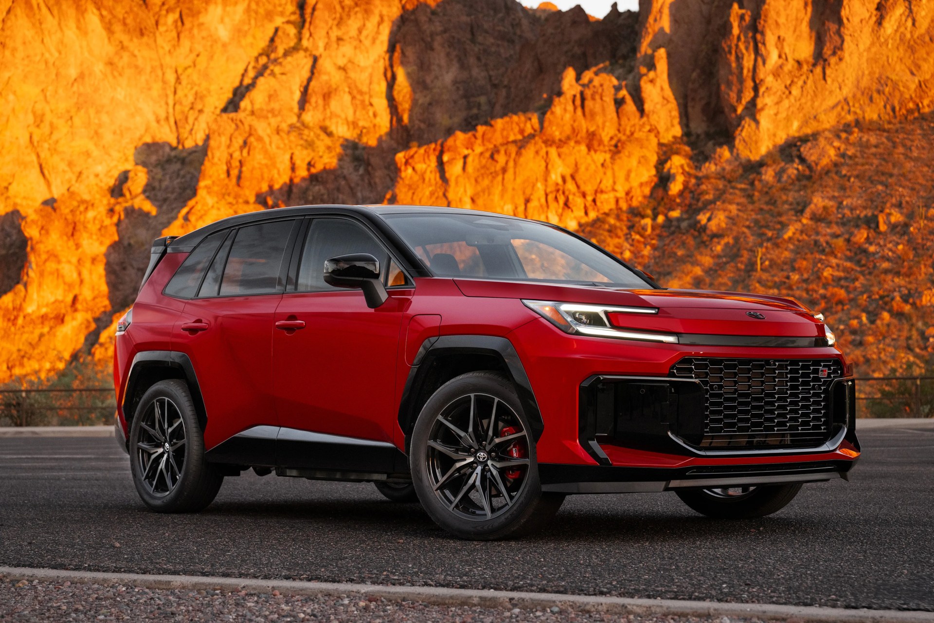 Red Toyota SUV with black roof and wheels parked on asphalt with orange rocky cliffs in the background.