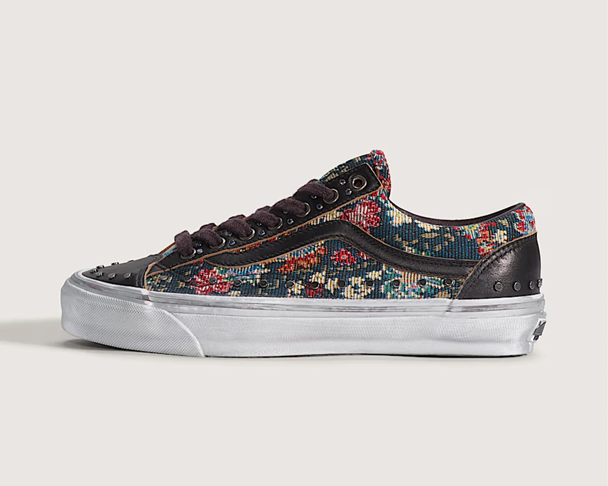Low-top sneaker with floral tapestry fabric, black leather accents, black laces, and white rubber sole.