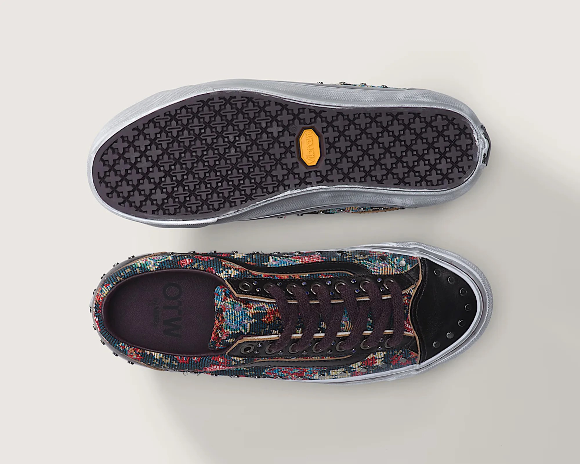 Pair of low-top sneakers with multicolor woven fabric uppers, black toe caps with studs, and black rubber soles shown from top and bottom.