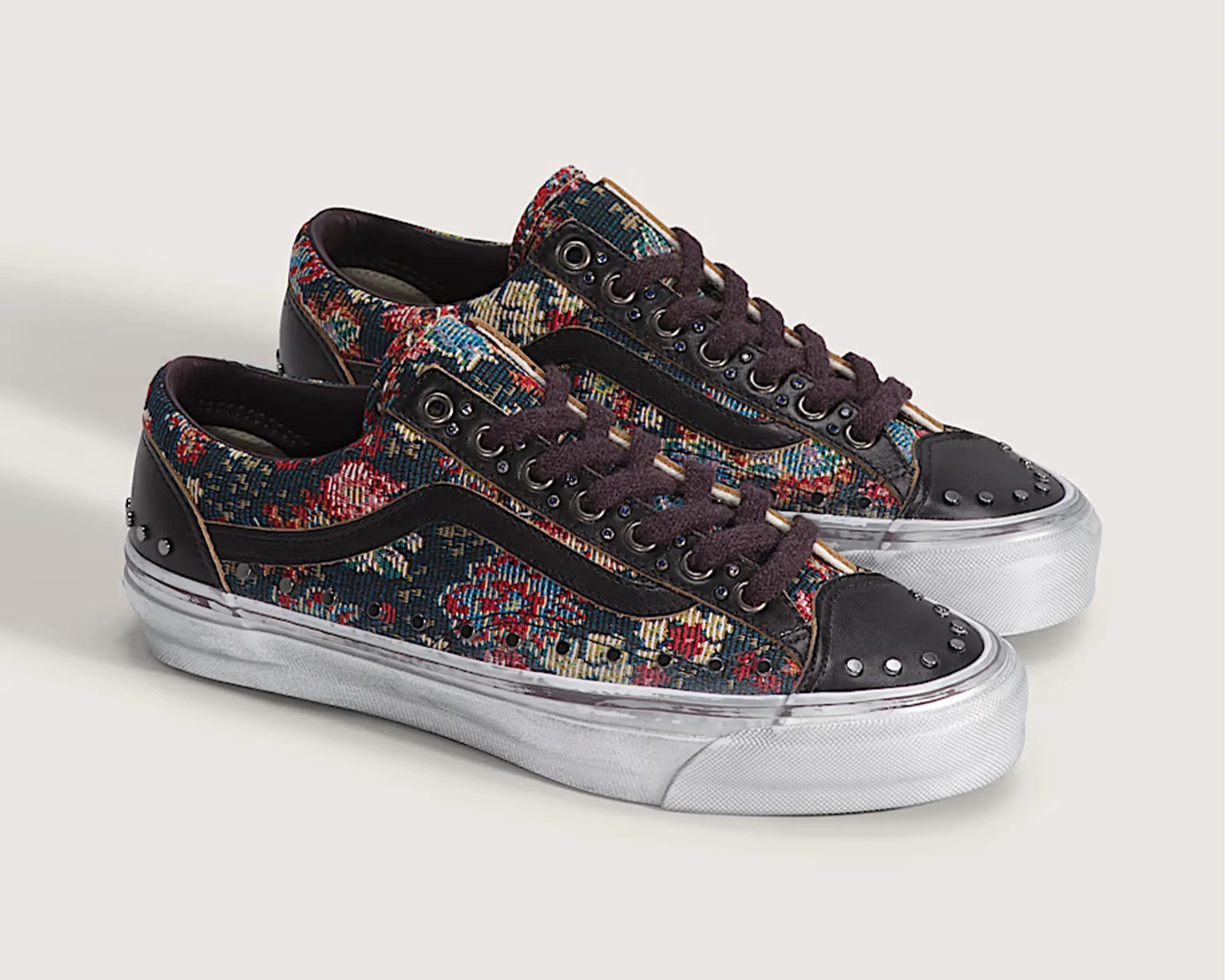 Pair of low-top sneakers with multicolor floral tapestry fabric, black leather accents, metal studs, and white rubber soles.