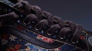 Close-up of black fuzzy shoelaces threaded through black eyelets on a multicolored woven fabric sneaker.