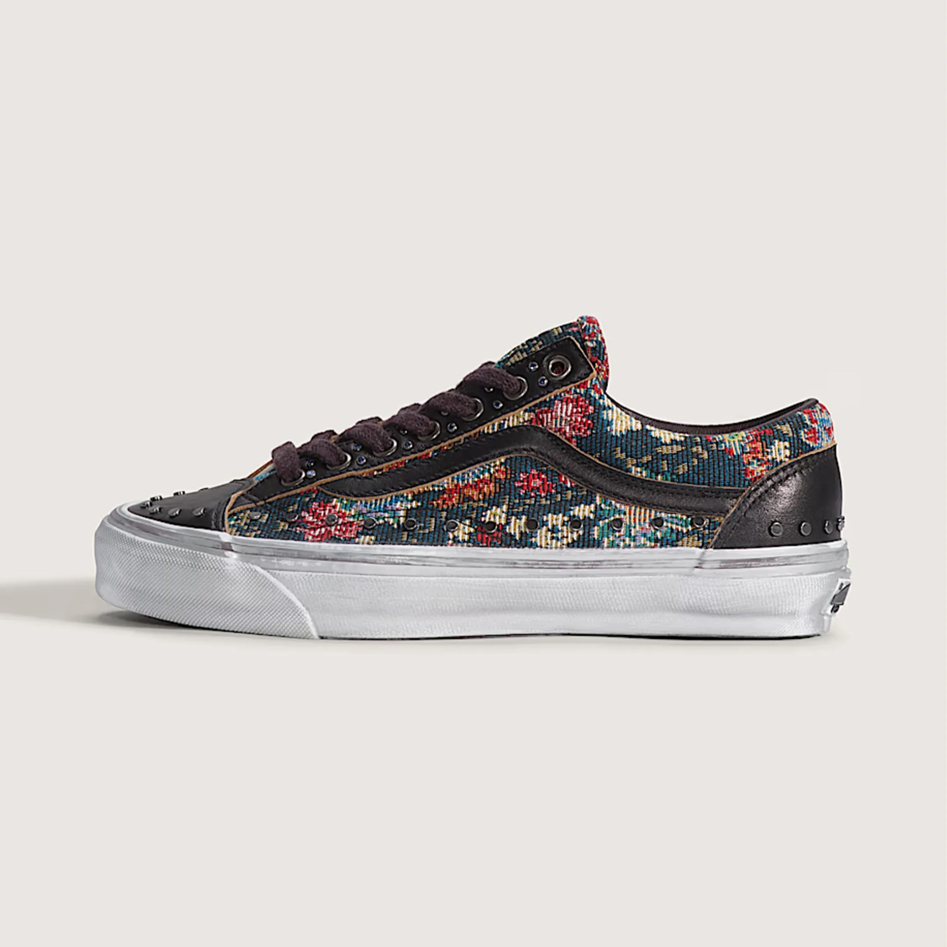 Low-top sneaker with floral tapestry fabric, black leather accents, black laces, and white rubber sole.