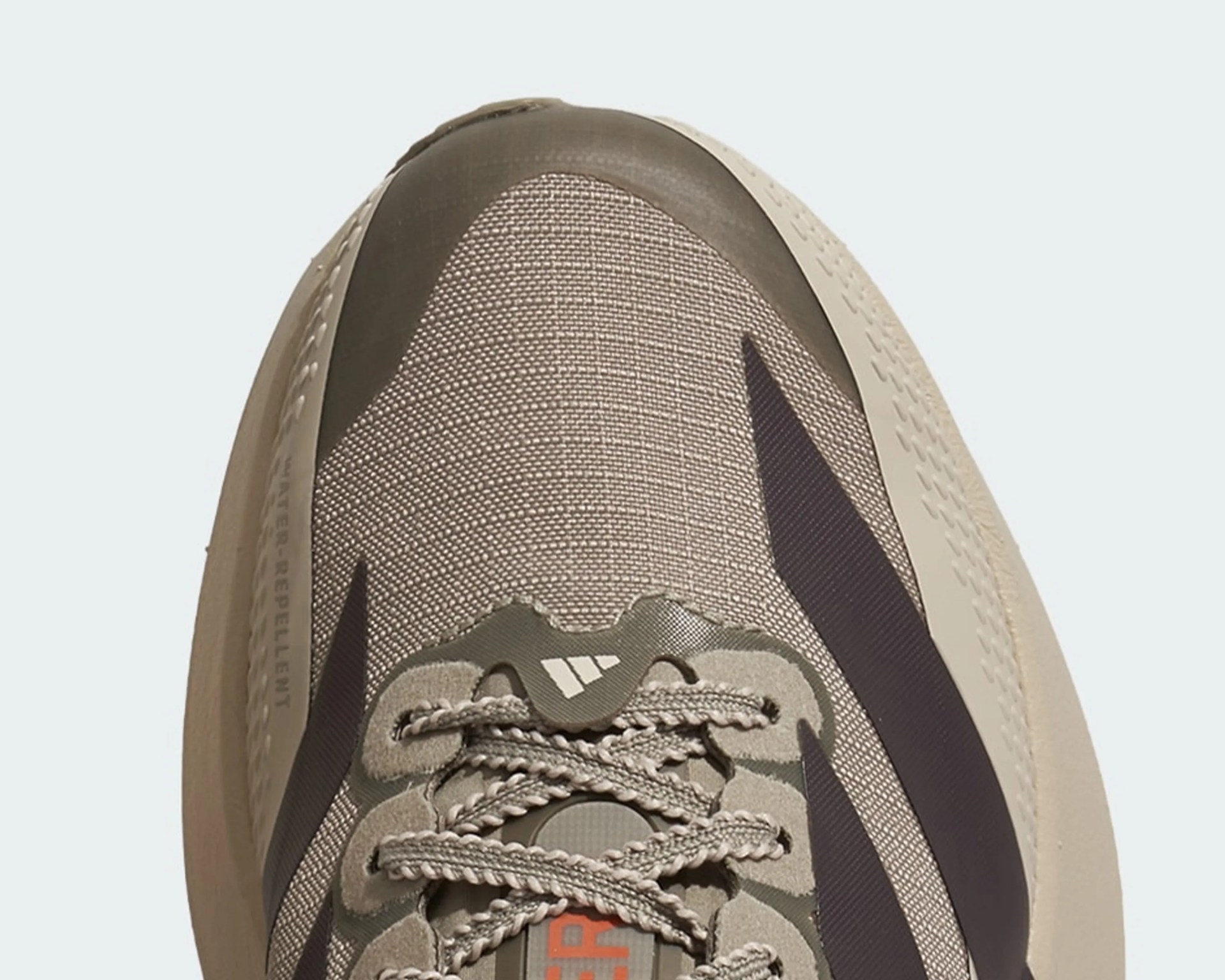 Close-up of the front part of a beige and dark brown Adidas sneaker with woven fabric and braided laces.