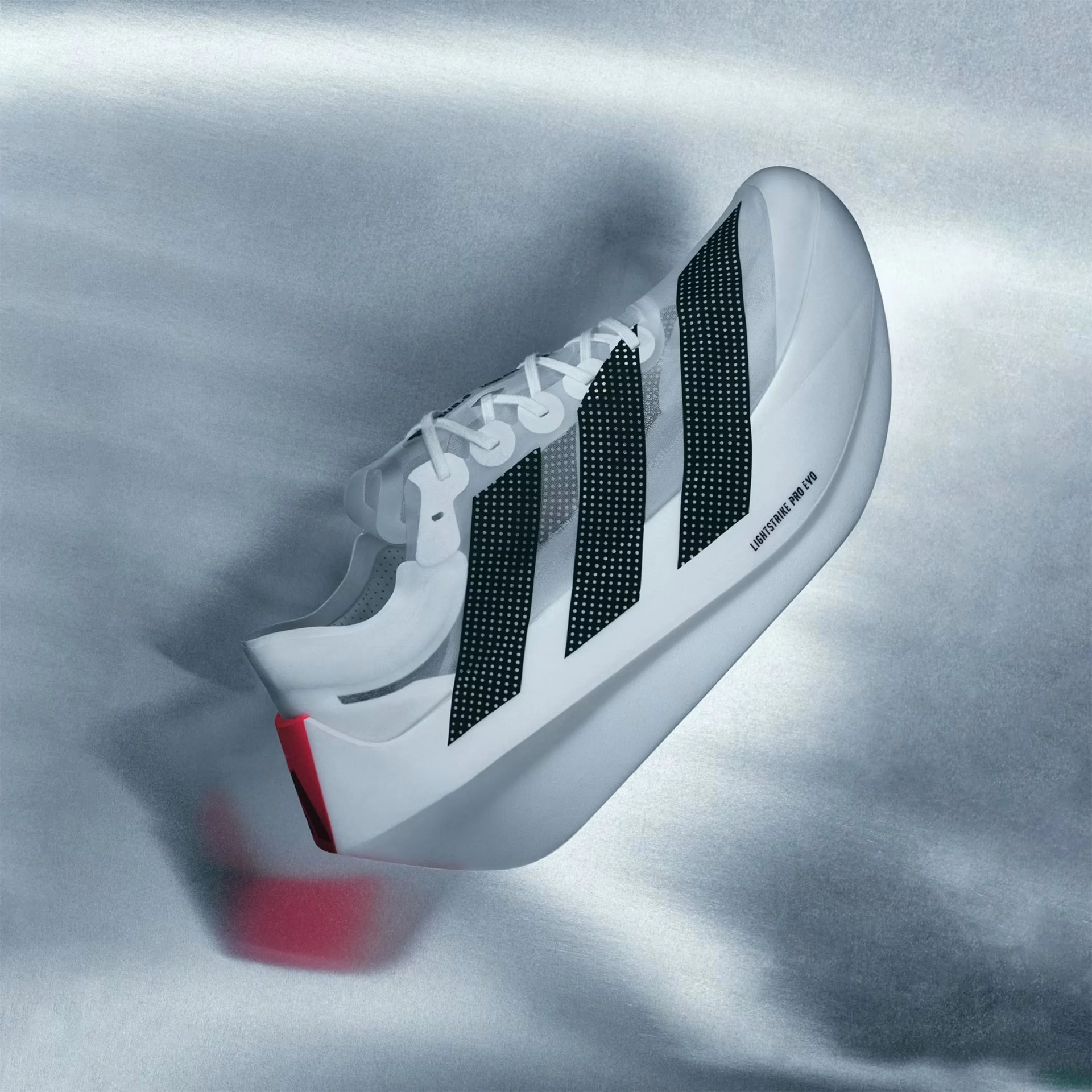 White Adidas Lightstrike Pro Evo sneaker with black dotted stripes and red heel detail on a silver surface.
