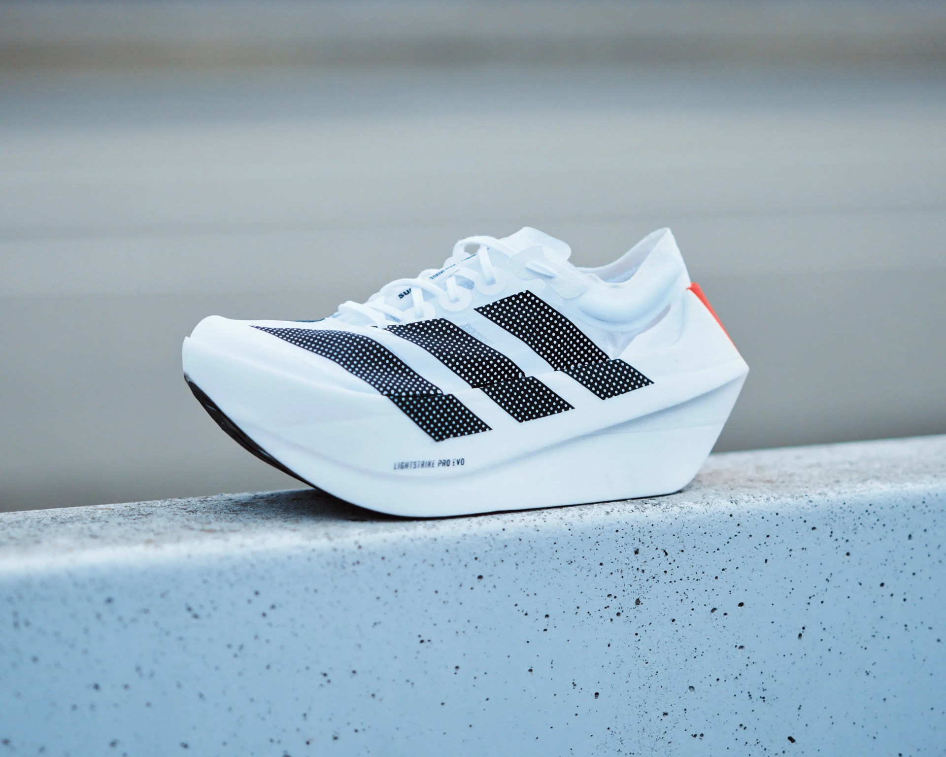 White Adidas running shoe with black stripes and thick sole on a concrete ledge.