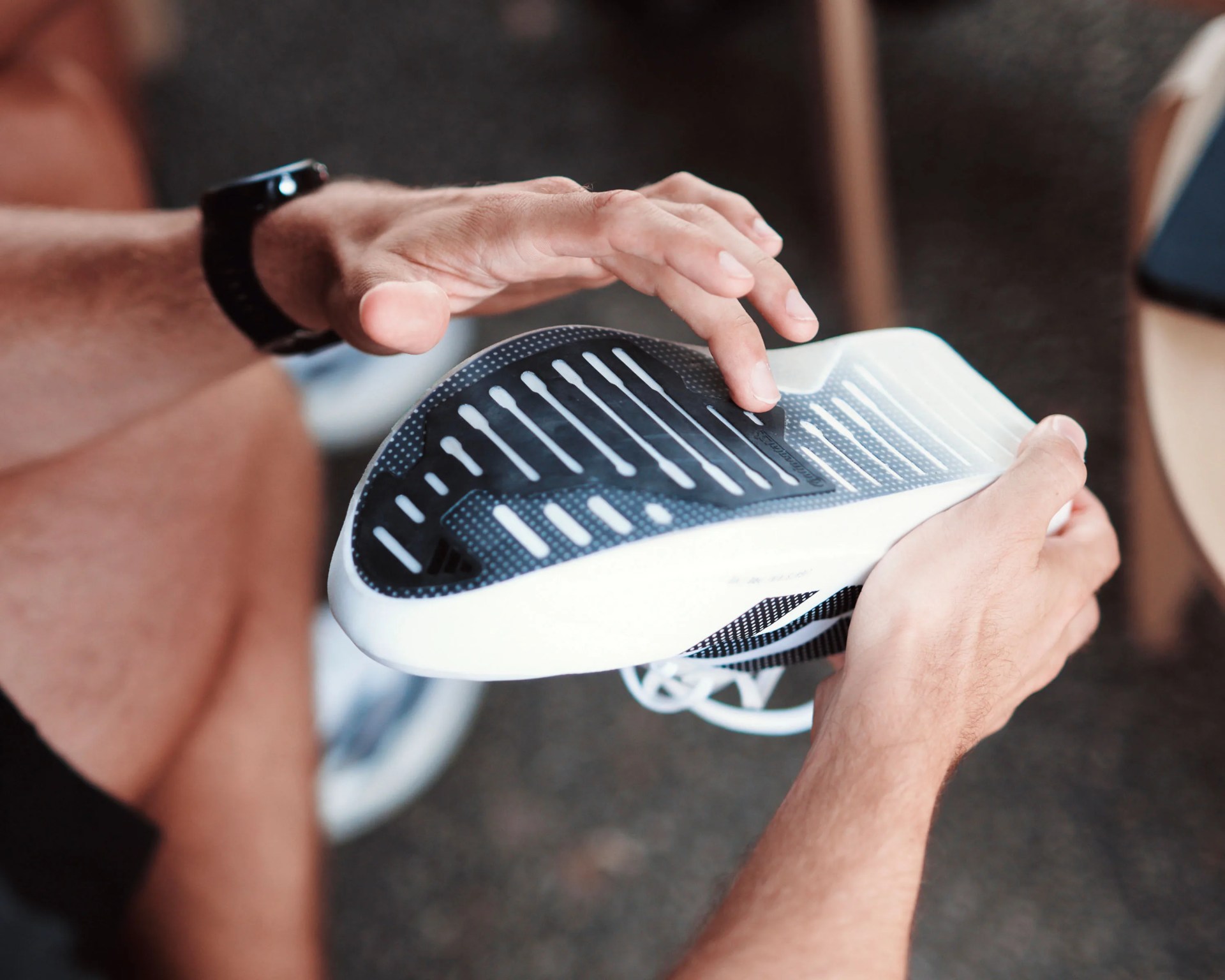 Person holding a white and black running shoe, showing the sole with grip patterns.