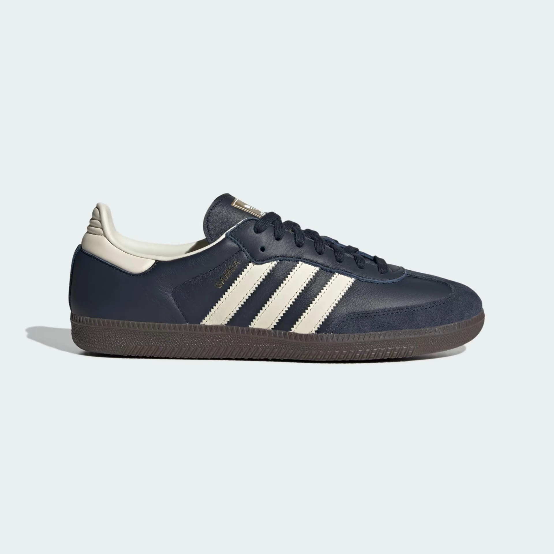 Navy blue Adidas Samba sneaker with white stripes and brown sole, side view.