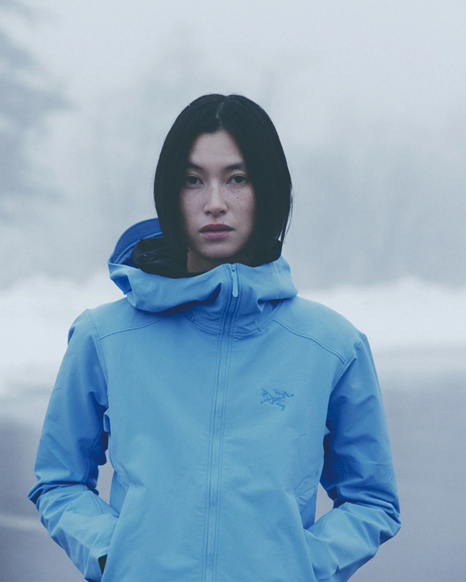 Woman wearing a light blue hooded jacket with a front zipper in a foggy outdoor setting.