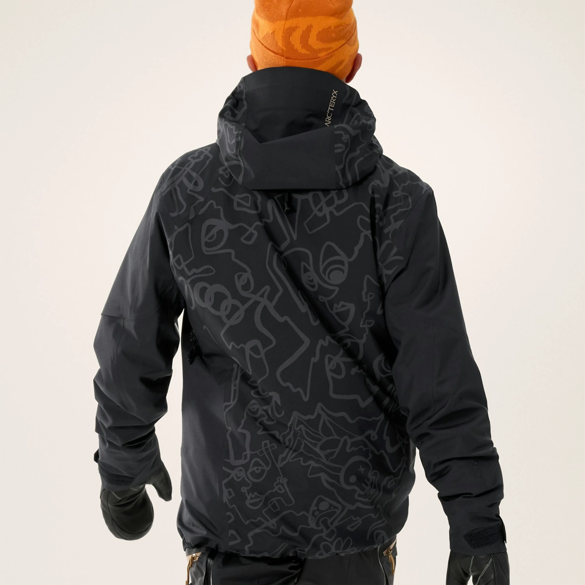 Black jacket with abstract line art pattern on the back worn by a person in an orange beanie and black gloves.