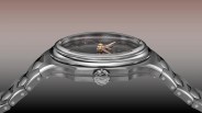 Side view of a stainless steel wristwatch with a black dial, gold hands, and a linked metal bracelet.
