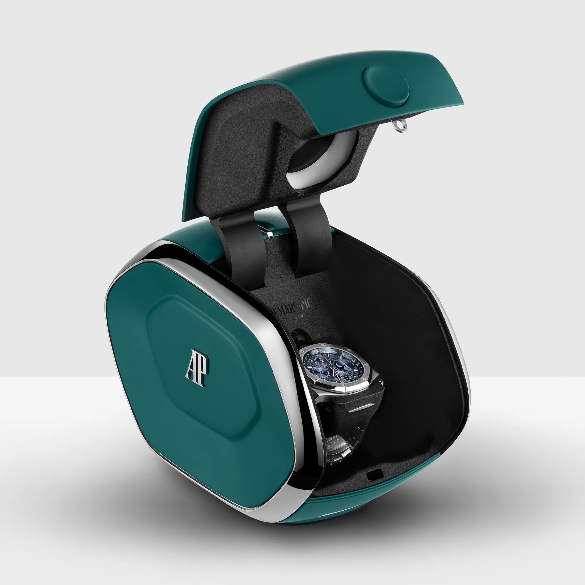 Teal and black watch winder with silver trim and "AP" logo, holding a silver watch with a blue dial inside.