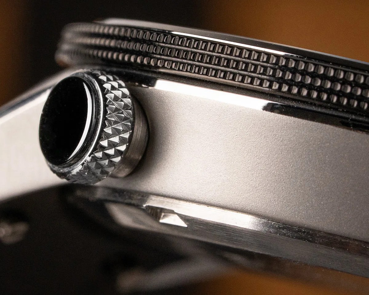 Close-up of a silver watch crown with textured grip and a ridged bezel edge.