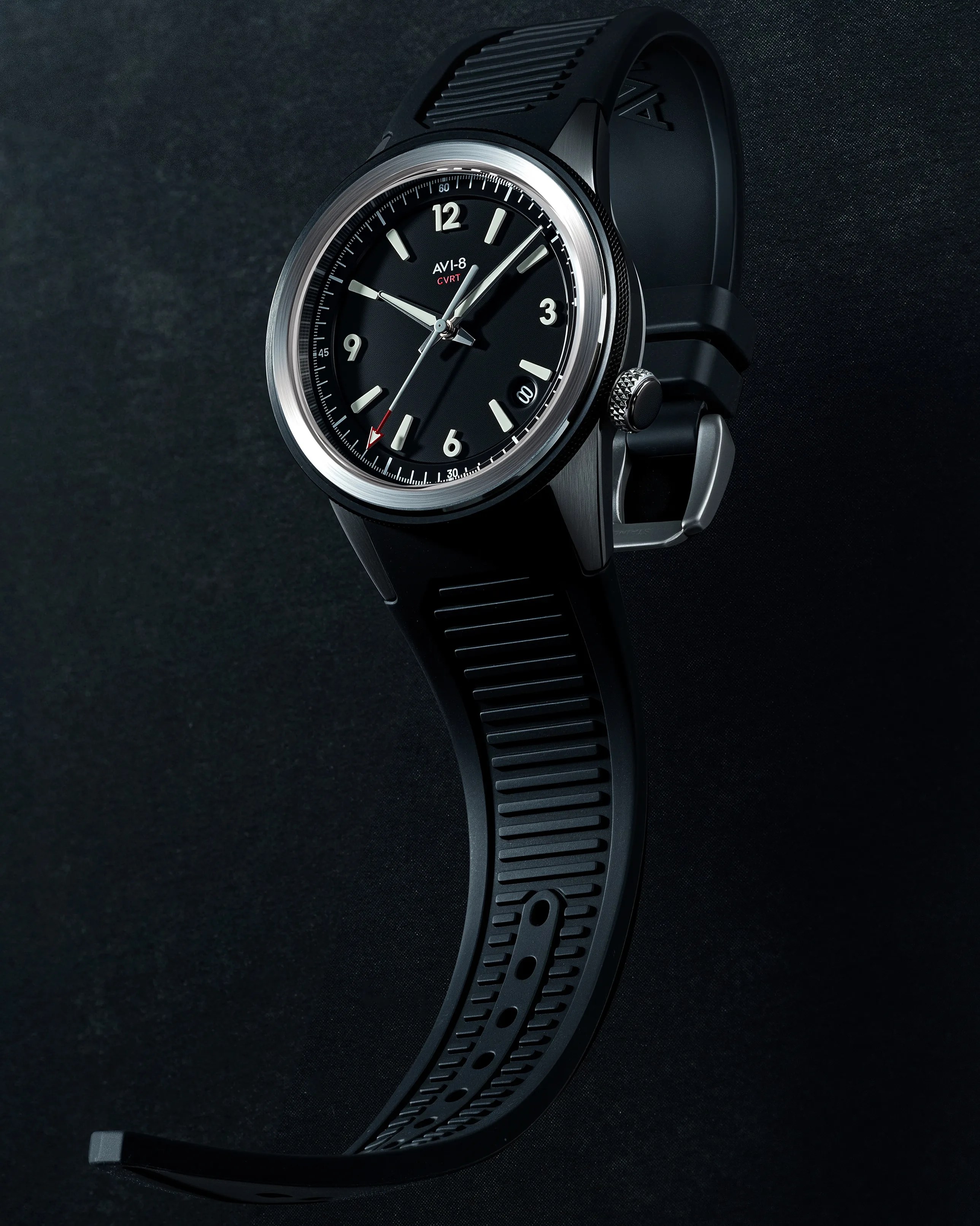 Black AVI-8 wristwatch with silver bezel, black dial, white hour markers, and black rubber strap on a dark background.