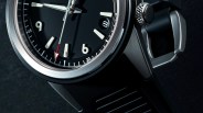 Close-up of a black watch face with white hour markers, a red-tipped second hand, and a brushed metal bezel.