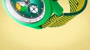 Green watch with yellow and green woven strap on a yellow background.