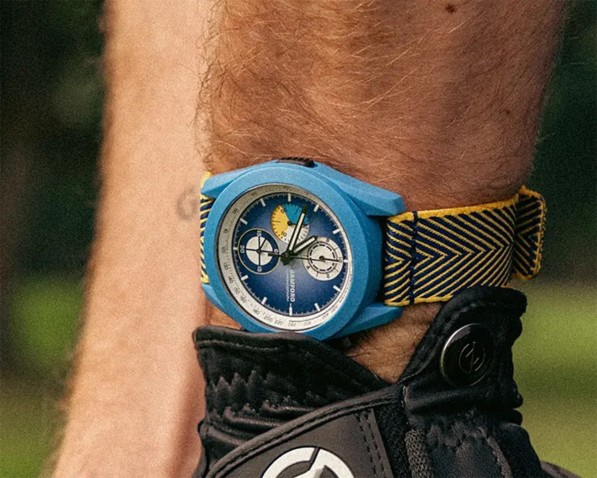 Blue wristwatch with a blue and yellow striped fabric strap worn above a black glove.