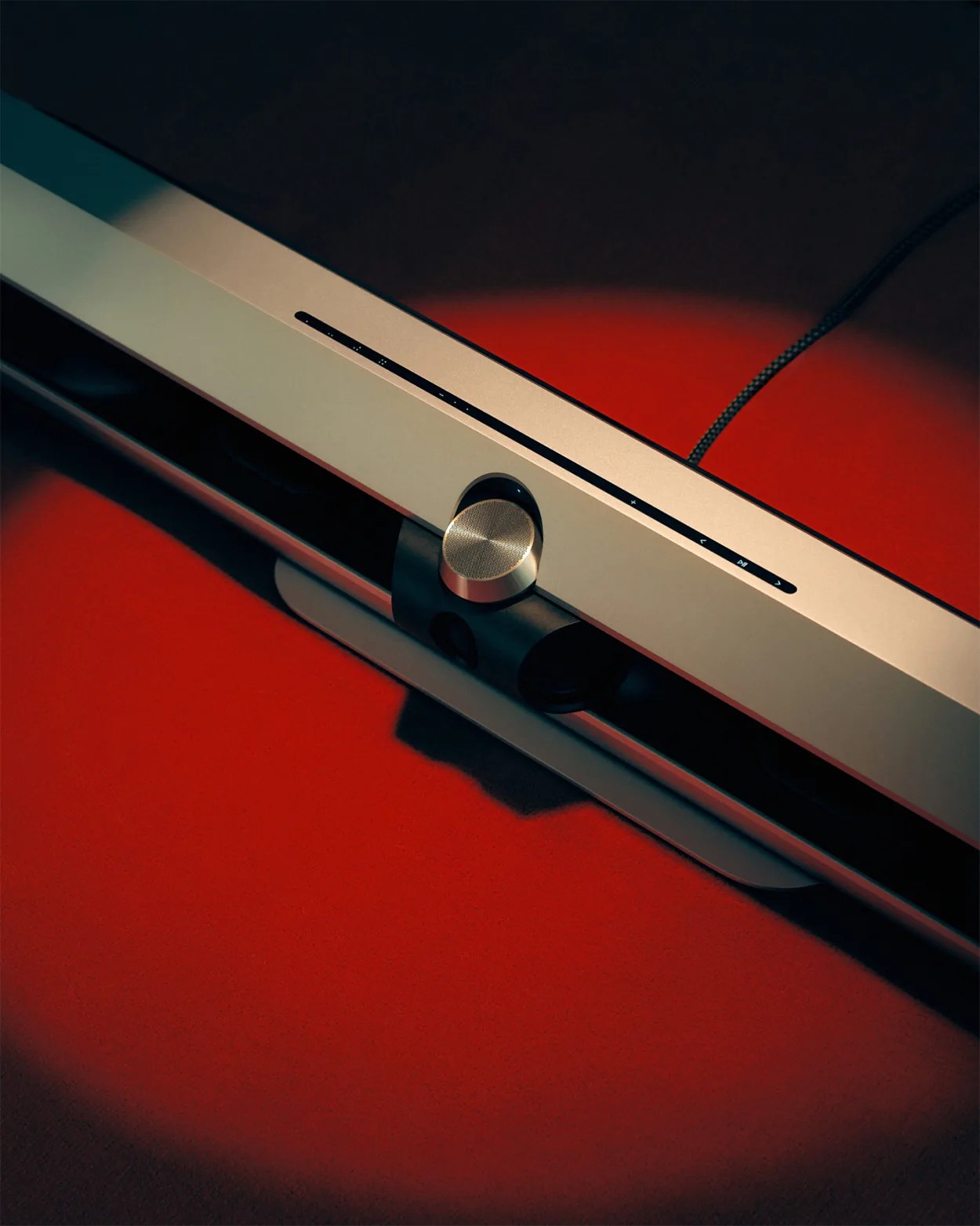 Silver soundbar with a central round volume knob on a red surface.