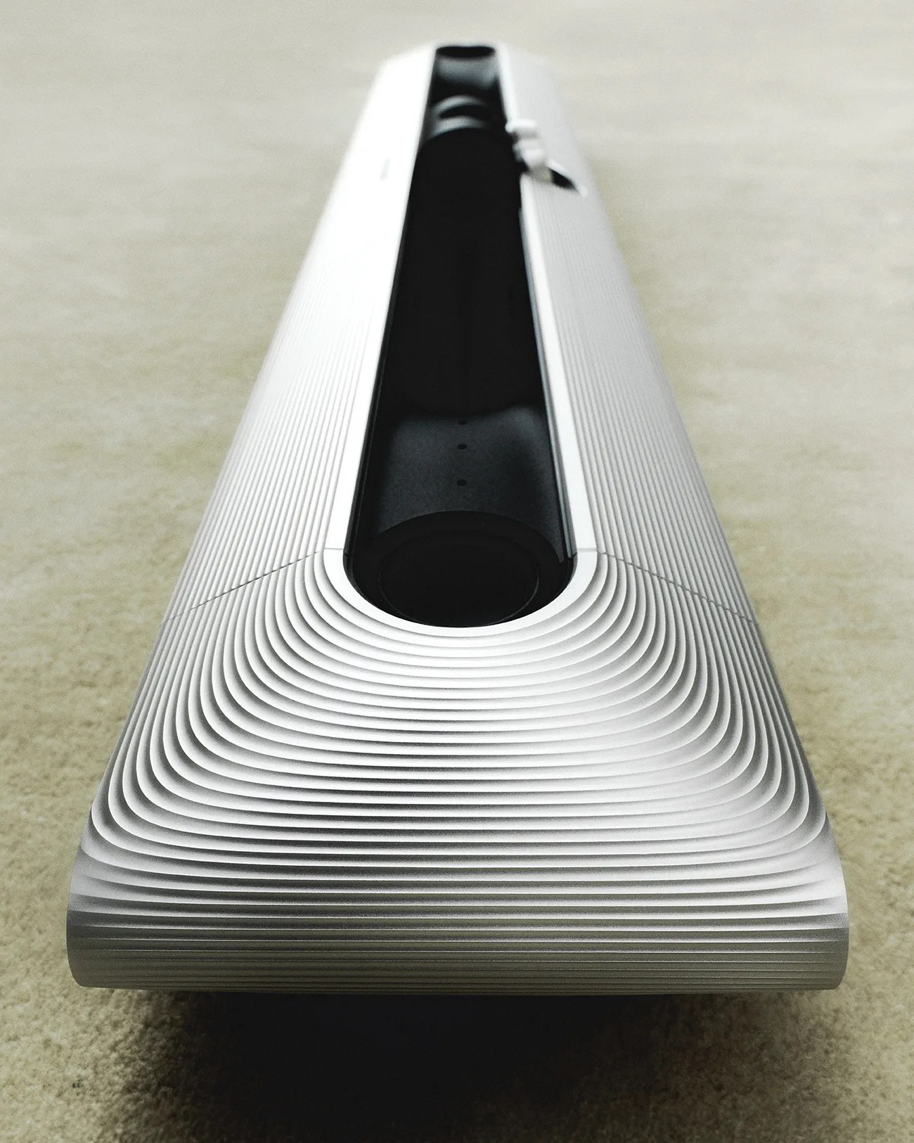 Silver soundbar with concentric ridged design on top, placed on a beige carpet.
