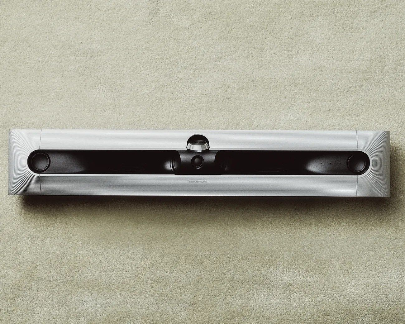 Silver and black Bang & Olufsen soundbar with a central volume knob on a beige carpet.