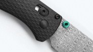 Close-up of a folding knife with a textured black handle and a patterned blade featuring a teal thumb stud.