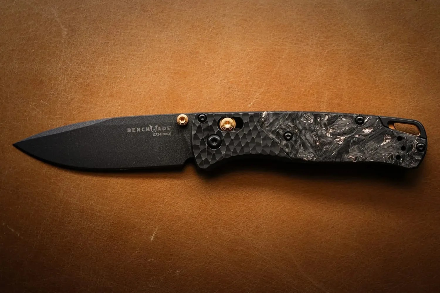 Black Benchmade folding knife with textured handle and gold accents on a brown leather surface.