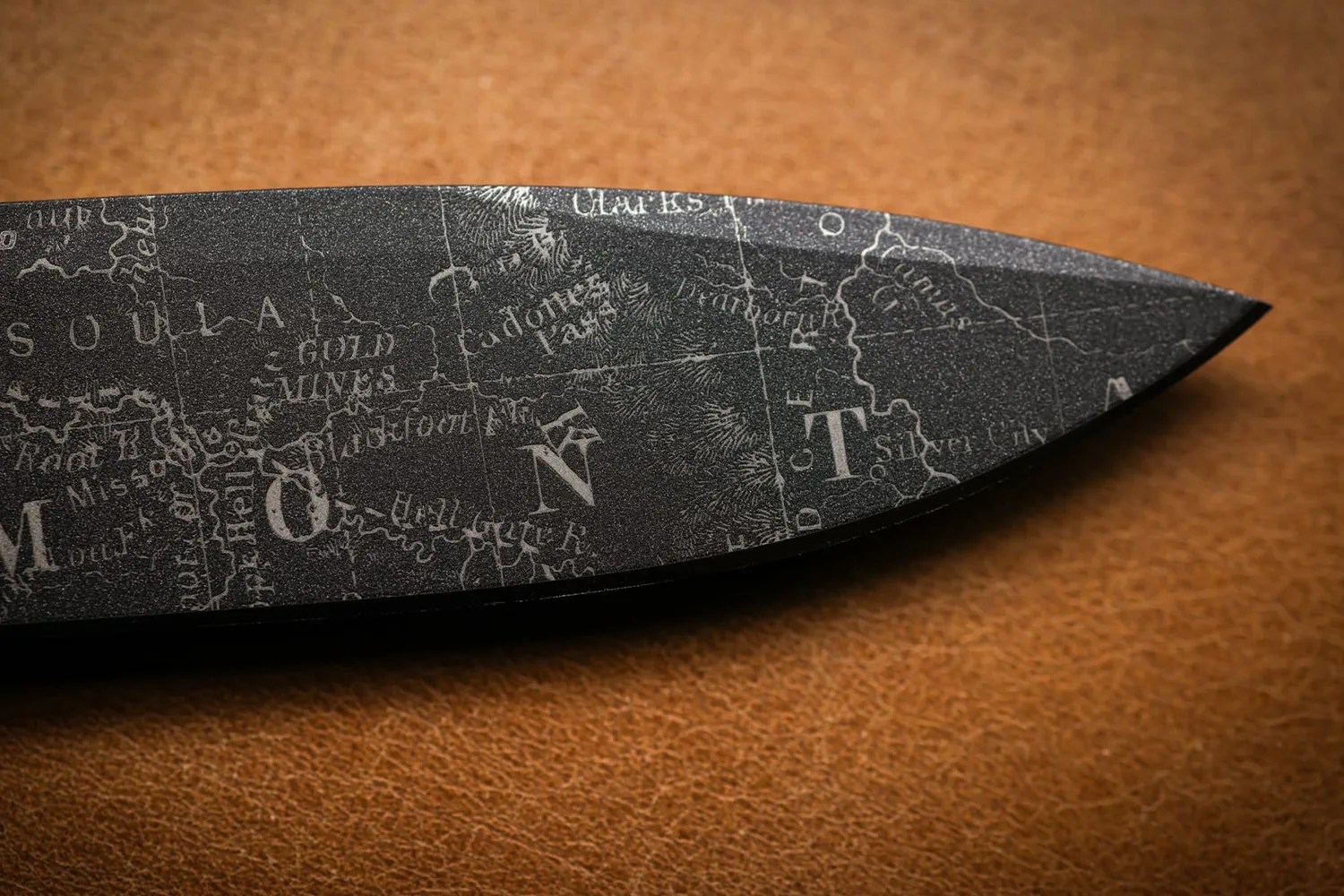 Close-up of a knife blade etched with a vintage map design showing parts of Montana and surrounding areas.
