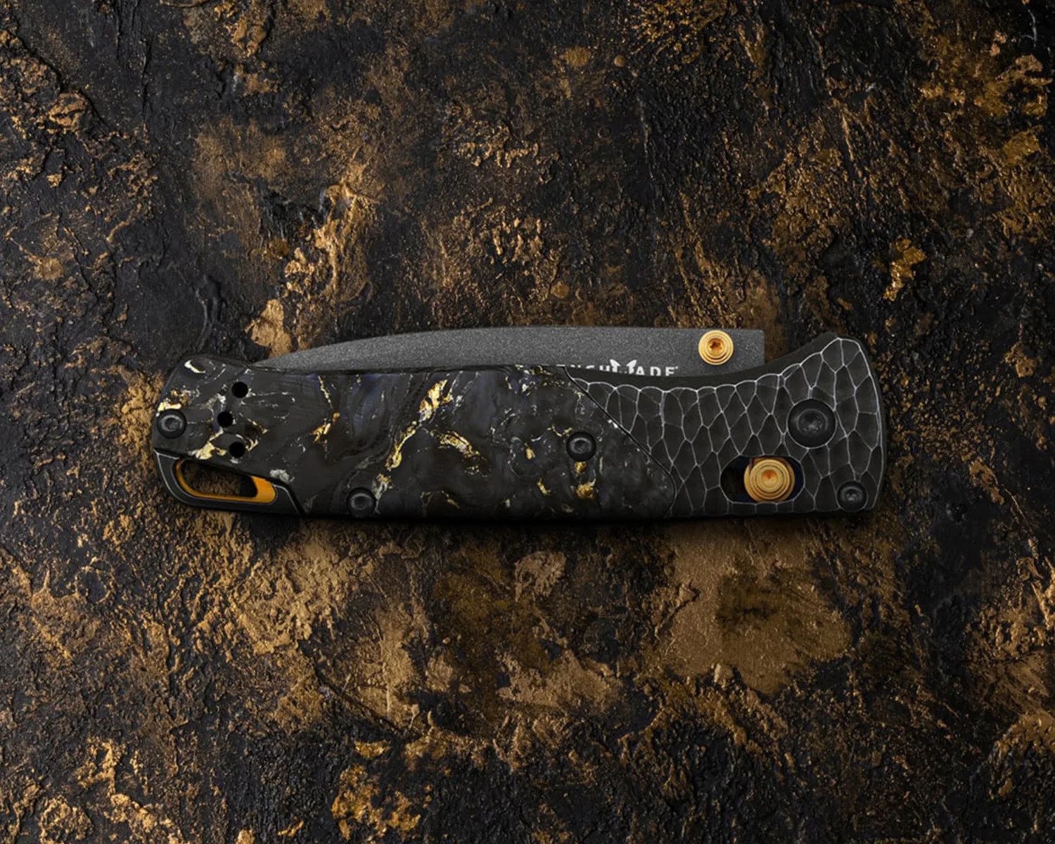 Folded black and gold folding knife with textured handle on a dark textured surface.