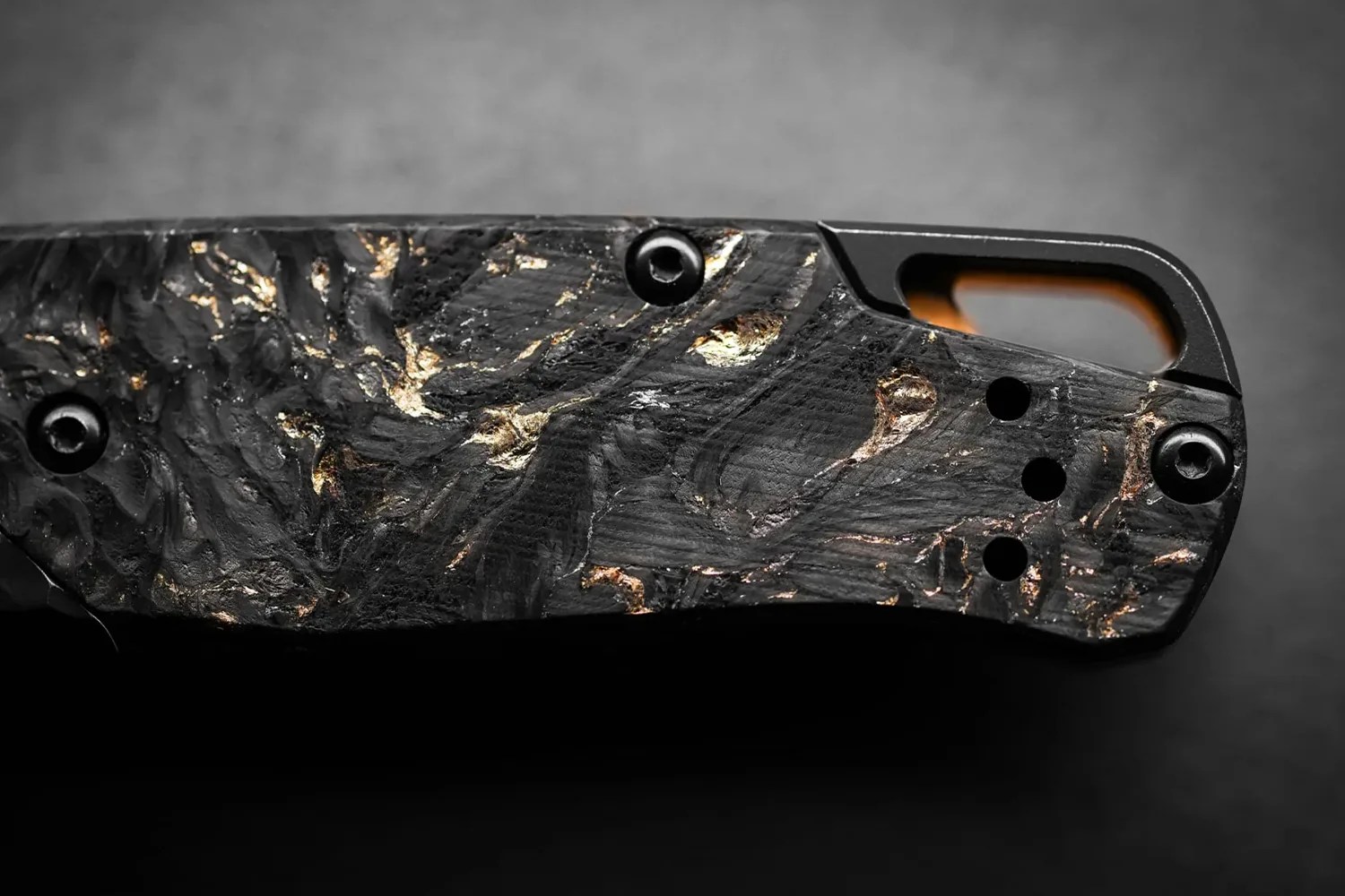 Close-up of a black textured knife handle with gold-colored metallic accents and three small holes near the end.