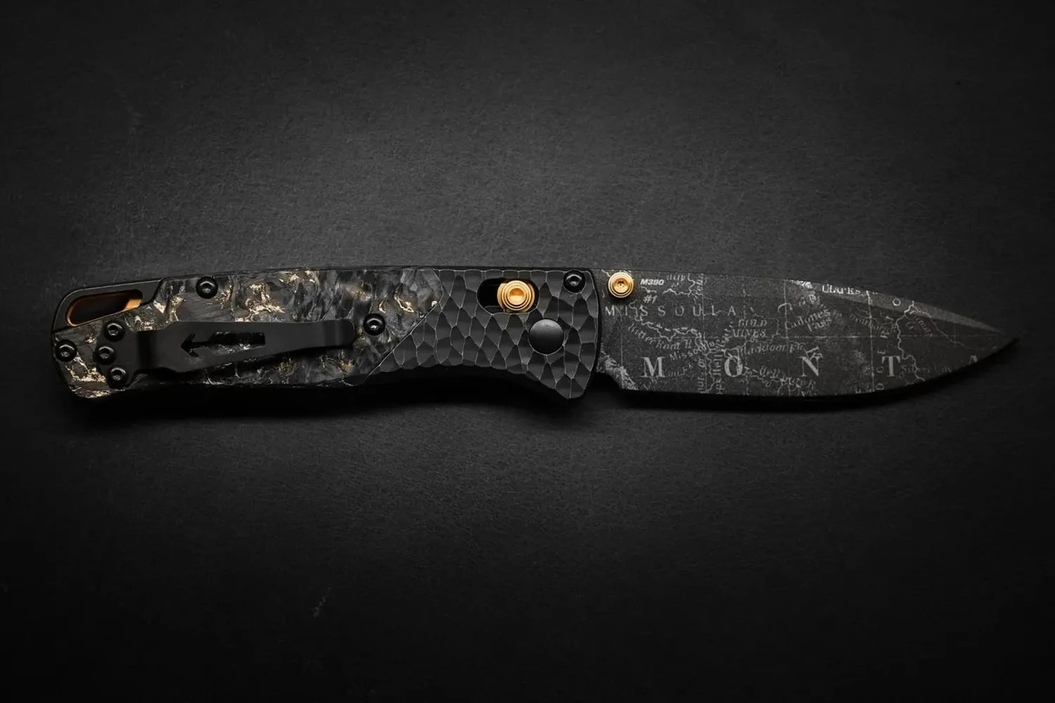 Black folding knife with a textured handle and a blade etched with a map design.