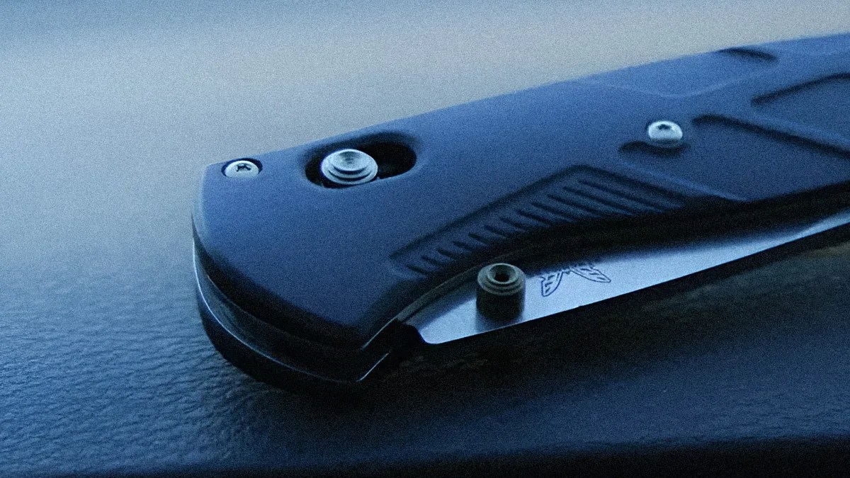 Close-up of a black folding knife with a partially visible silver blade resting on a textured dark surface.