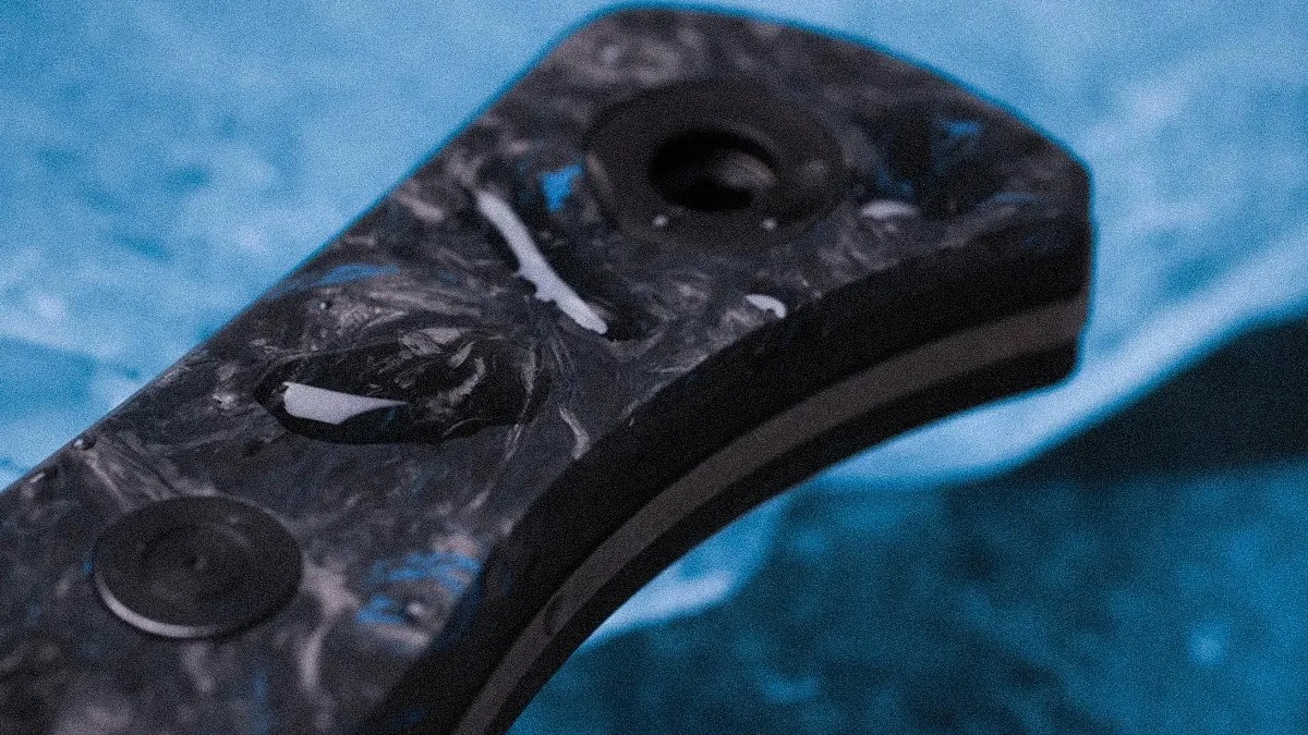 Close-up of a black and gray marbled knife handle with two screws on a blue textured surface.