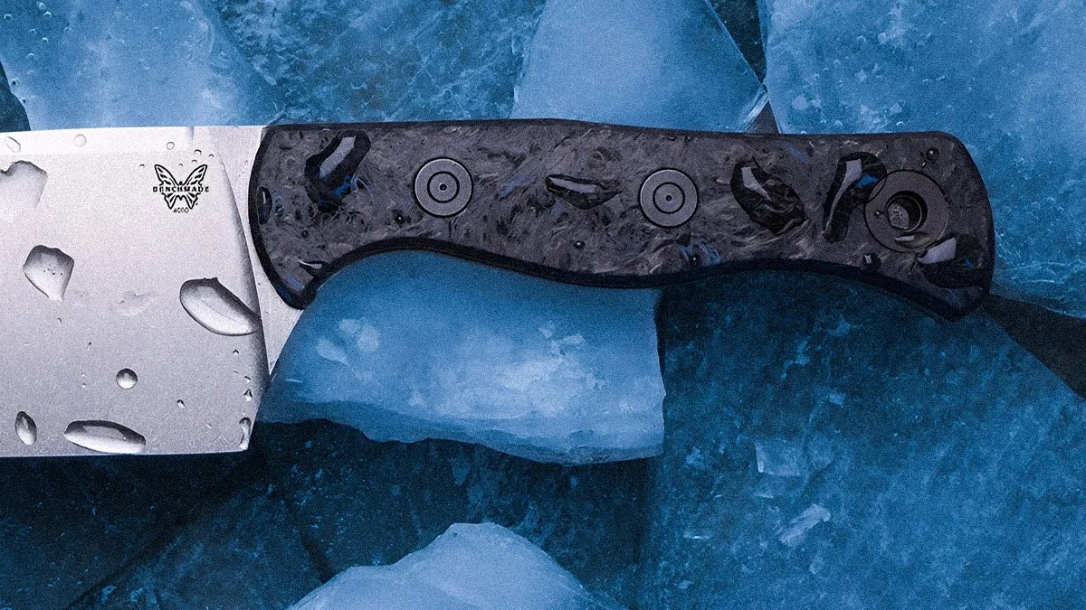 Benchmade knife with a textured dark handle and water droplets on the blade, resting on blue ice.