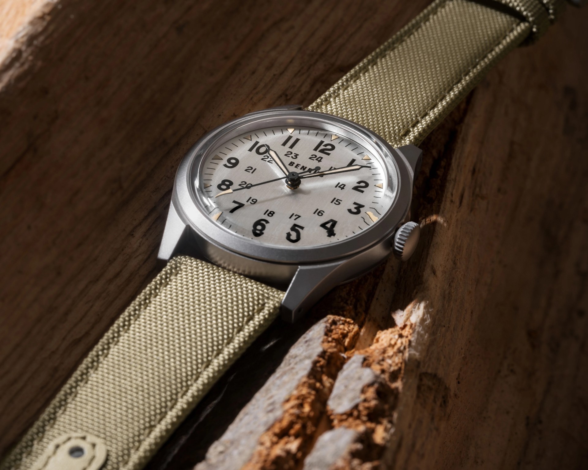Silver wristwatch with black numerals and beige fabric strap on a wooden surface.