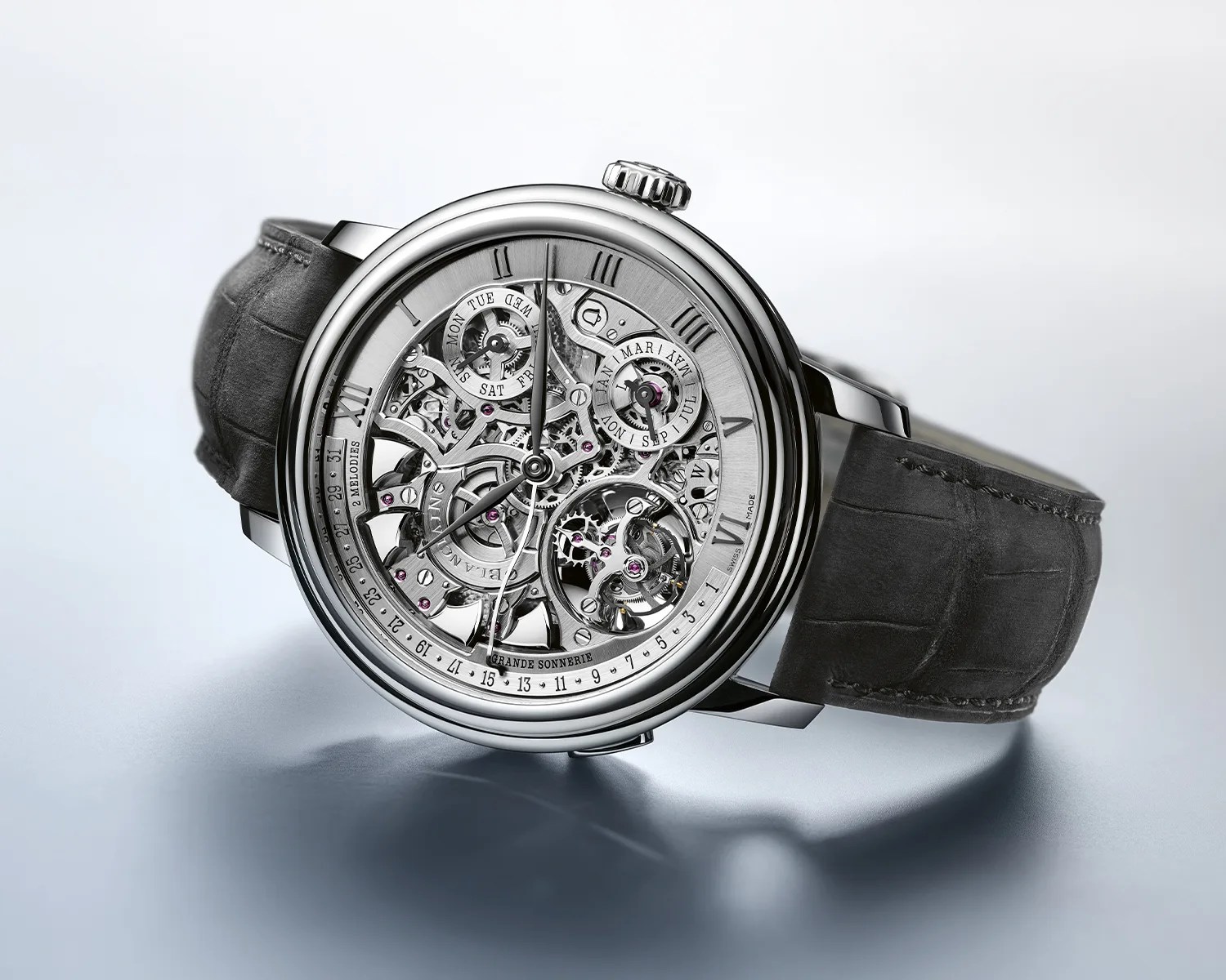 Skeleton dial luxury wristwatch with visible gears, silver case, and dark gray leather strap on a reflective surface.