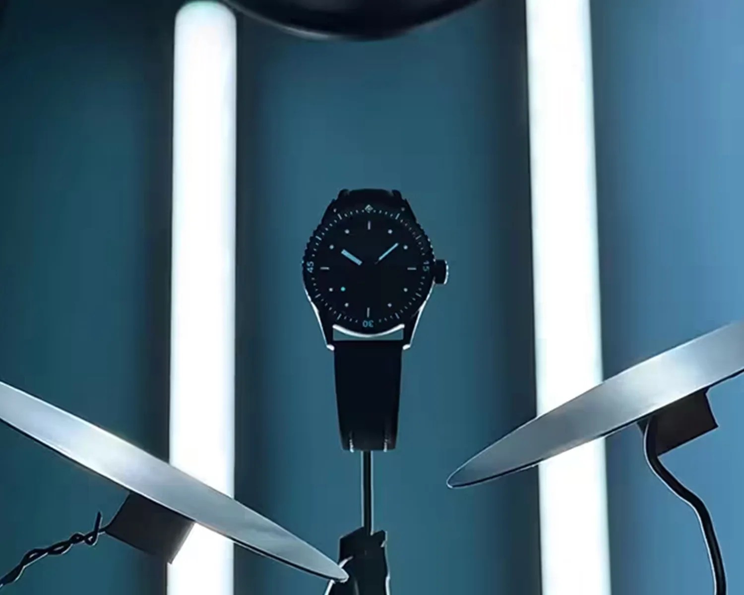 blue wristwatch with a round dial and blue strap displayed between two metallic cymbals against a blue background.