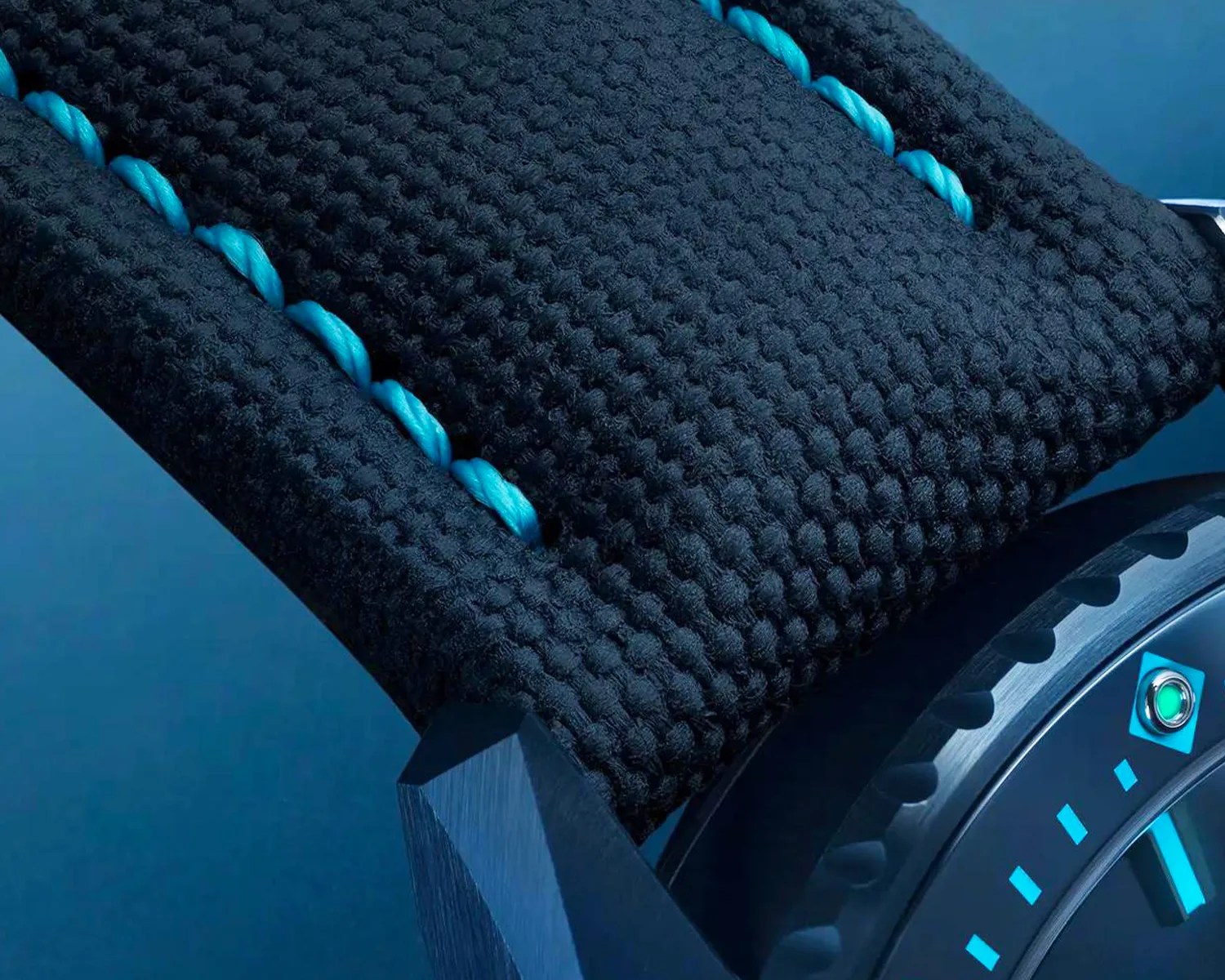 Close-up of a blue textured watch strap with blue stitching attached to a blue watch case and bezel.