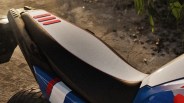 Close-up of a motorcycle seat with a white top, black sides, and three red rubber strips near the rear.