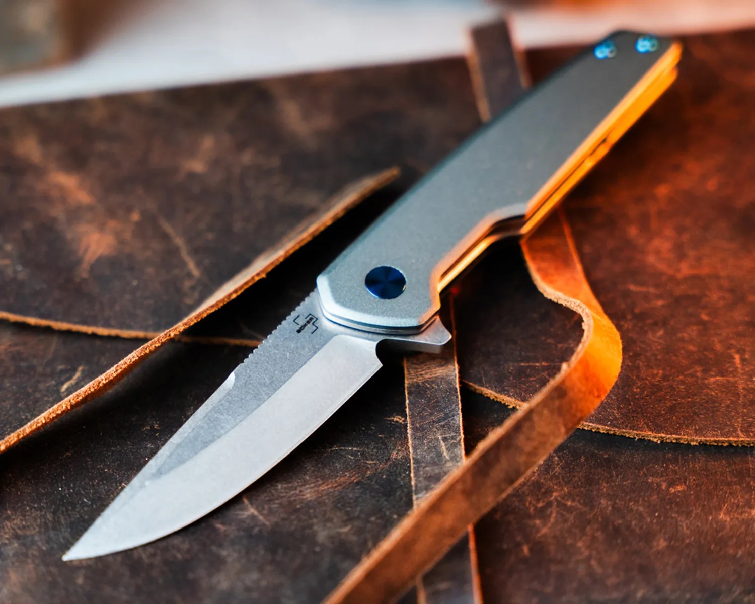Folding knife with a stonewashed blade and gray handle resting on a brown leather surface.