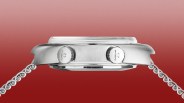 Side view of a silver metal watch case with two crowns and a linked metal bracelet against a red gradient background.