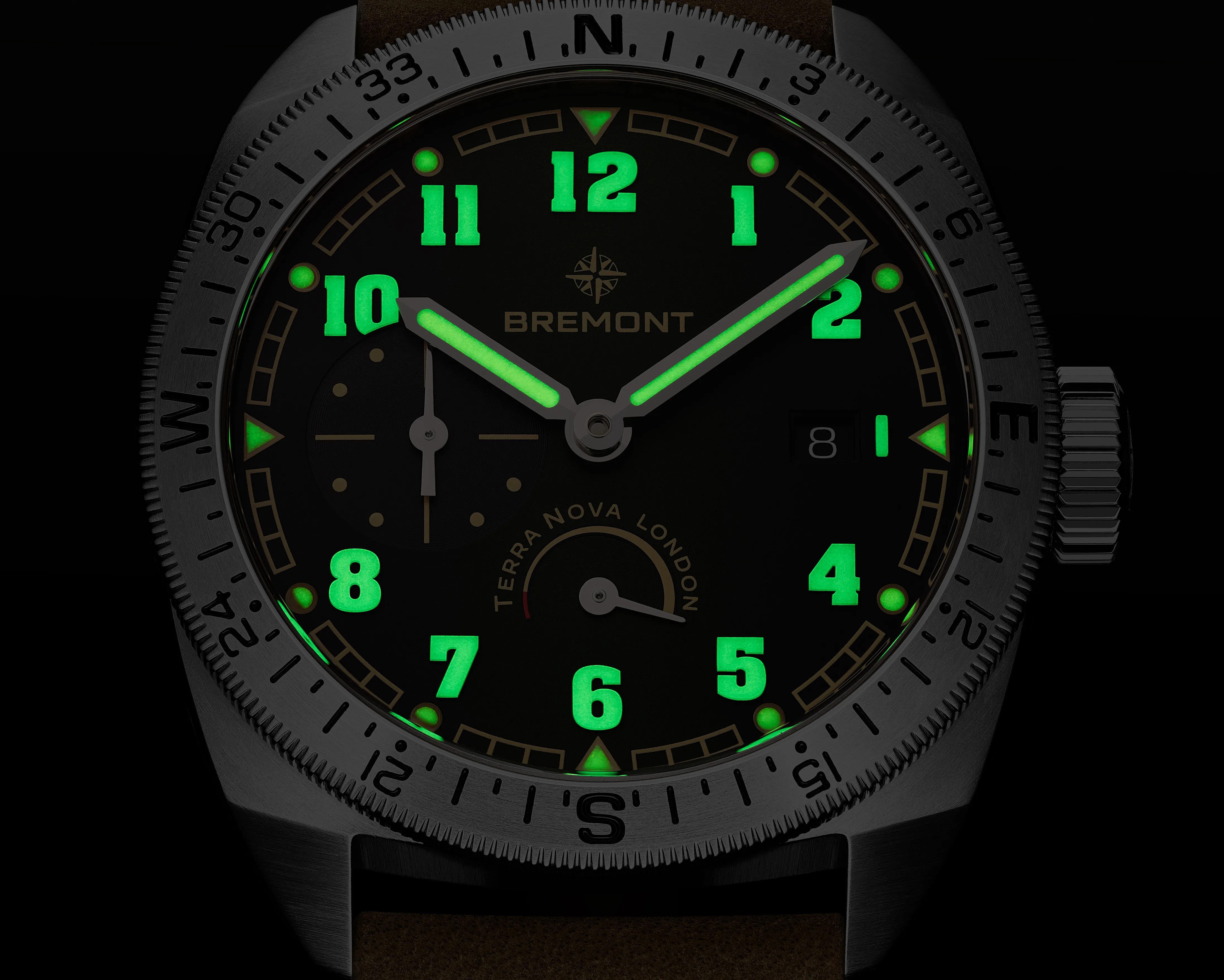 Close-up of a Bremont watch face with glowing green numerals and hands, compass bezel, and brown strap.