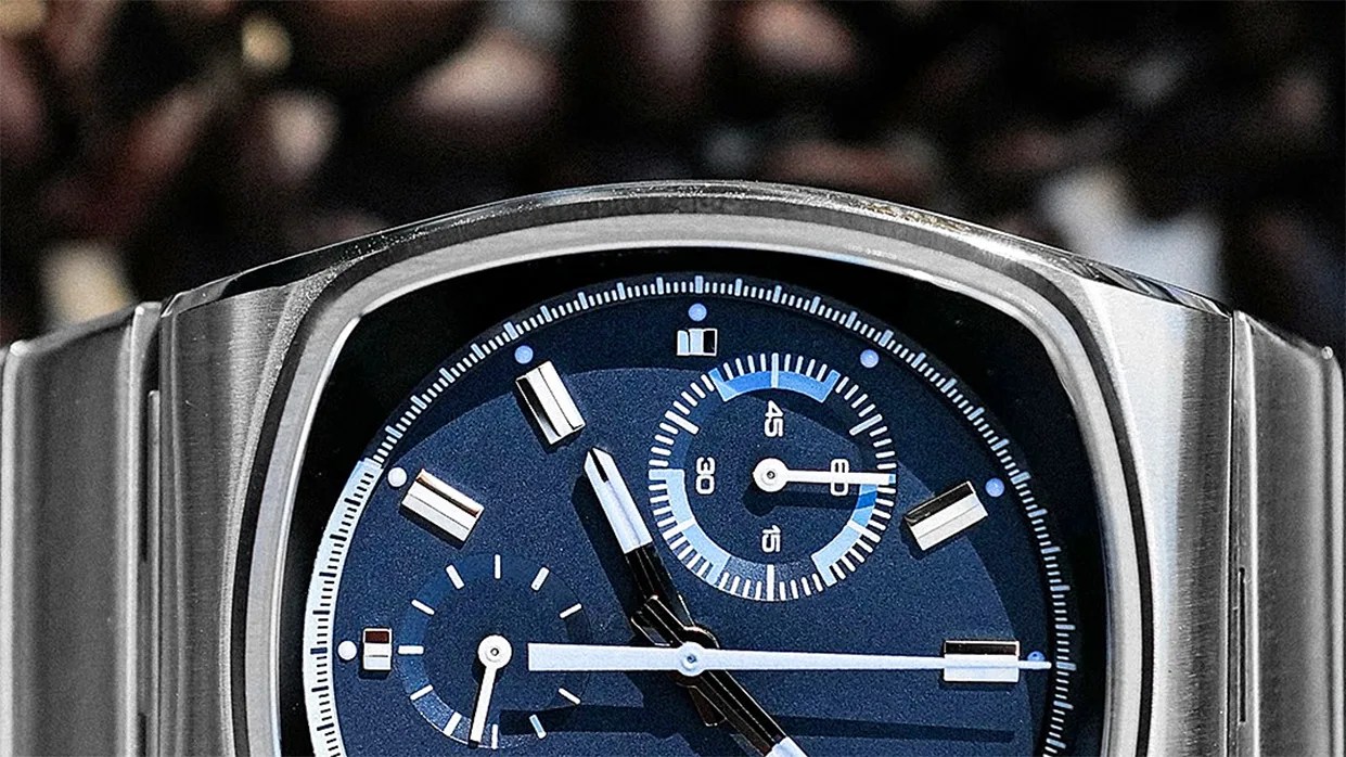 Close-up of a silver metal wristwatch with a blue dial featuring chronograph subdials and rectangular hour markers.